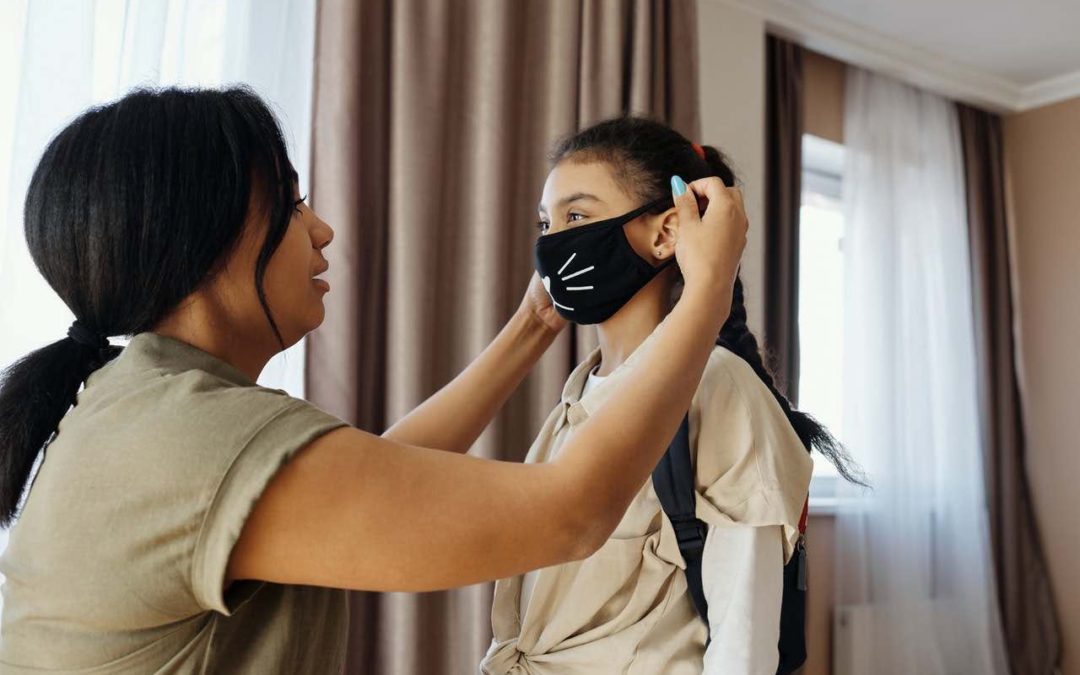 Mother preparing her daughter for school with a mask with cat whiskers
